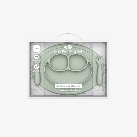Boxed Ezpz Mini Feeding Set in Sage displayed in retail packaging with the mat and utensils visible through the clear front.