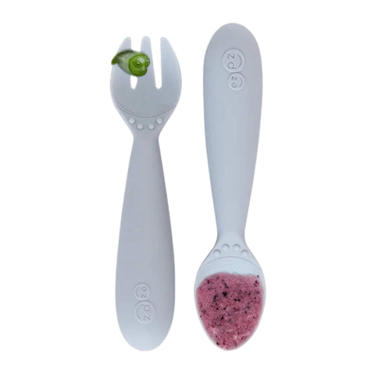 Pewter grey silicone toddler fork holding a piece of broccoli next to a matching spoon filled with vegetable puree.