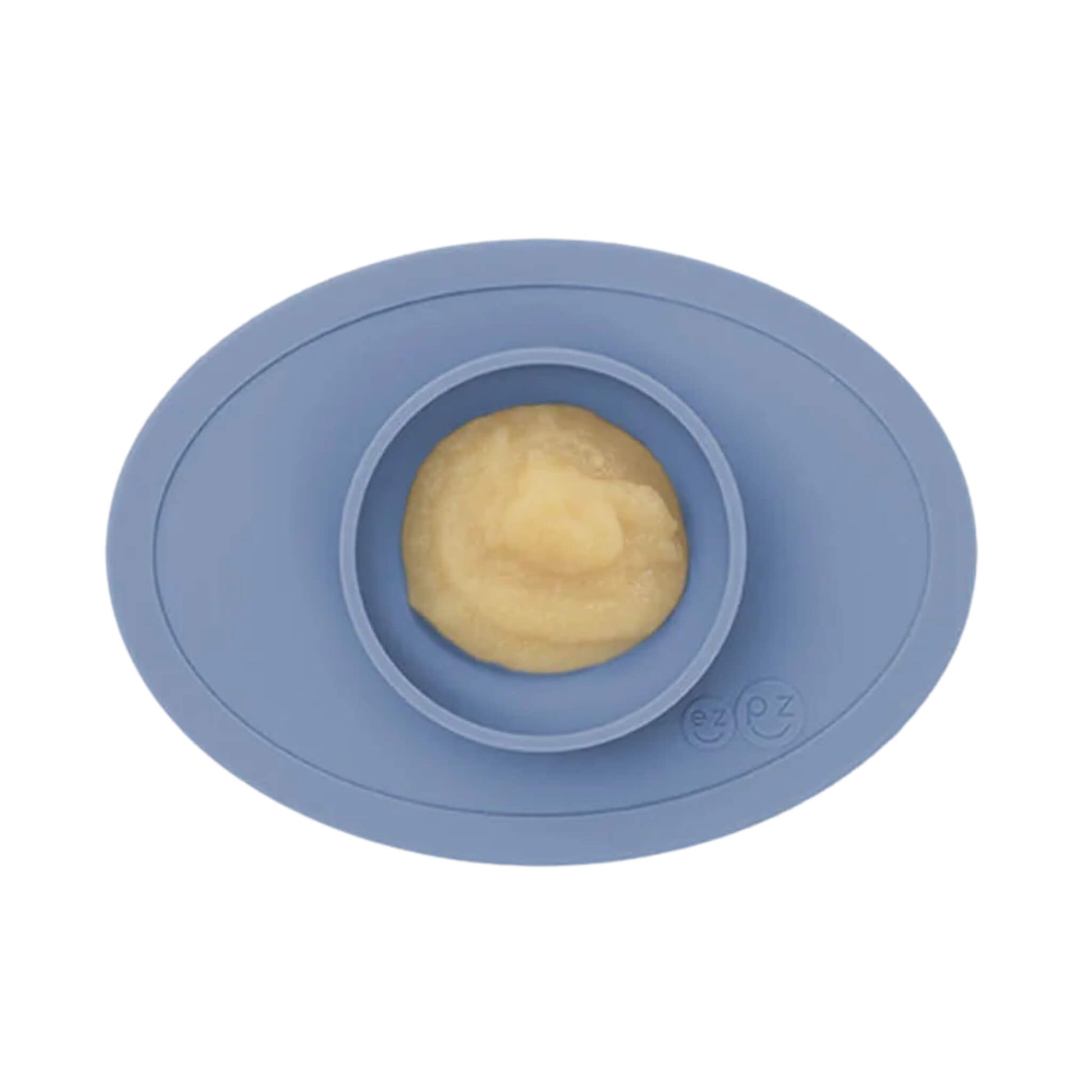 Indigo silicone suction placemat with built-in bowl, shown filled with a serving of smooth baby food.