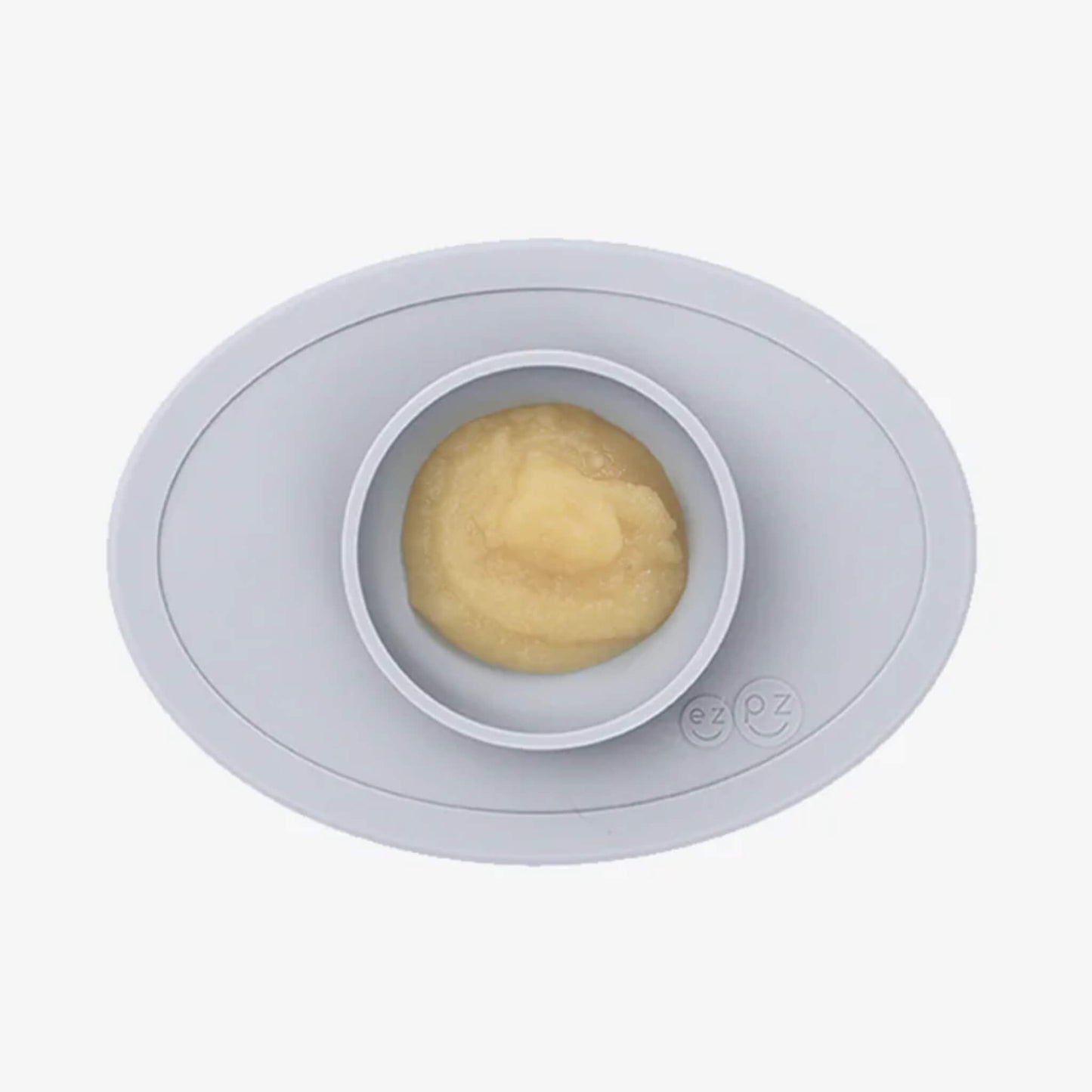 A grey silicone placemat with a small round bowl filled with smooth yellow puree, shown from above.