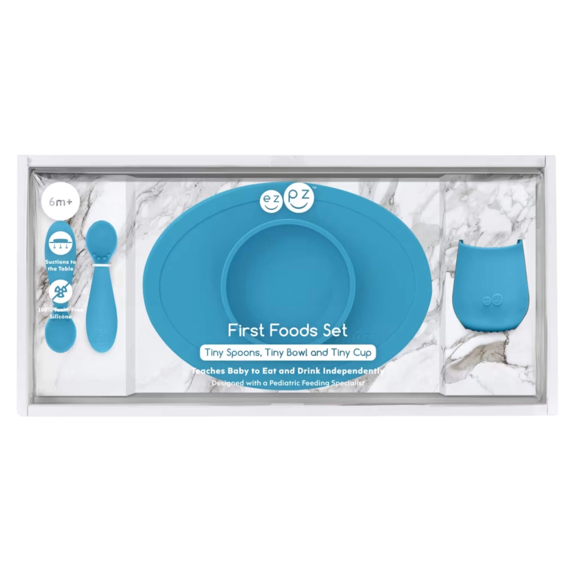 Boxed baby feeding set in blue showing a suction bowl, open cup and training spoons inside clear retail packaging with product details.