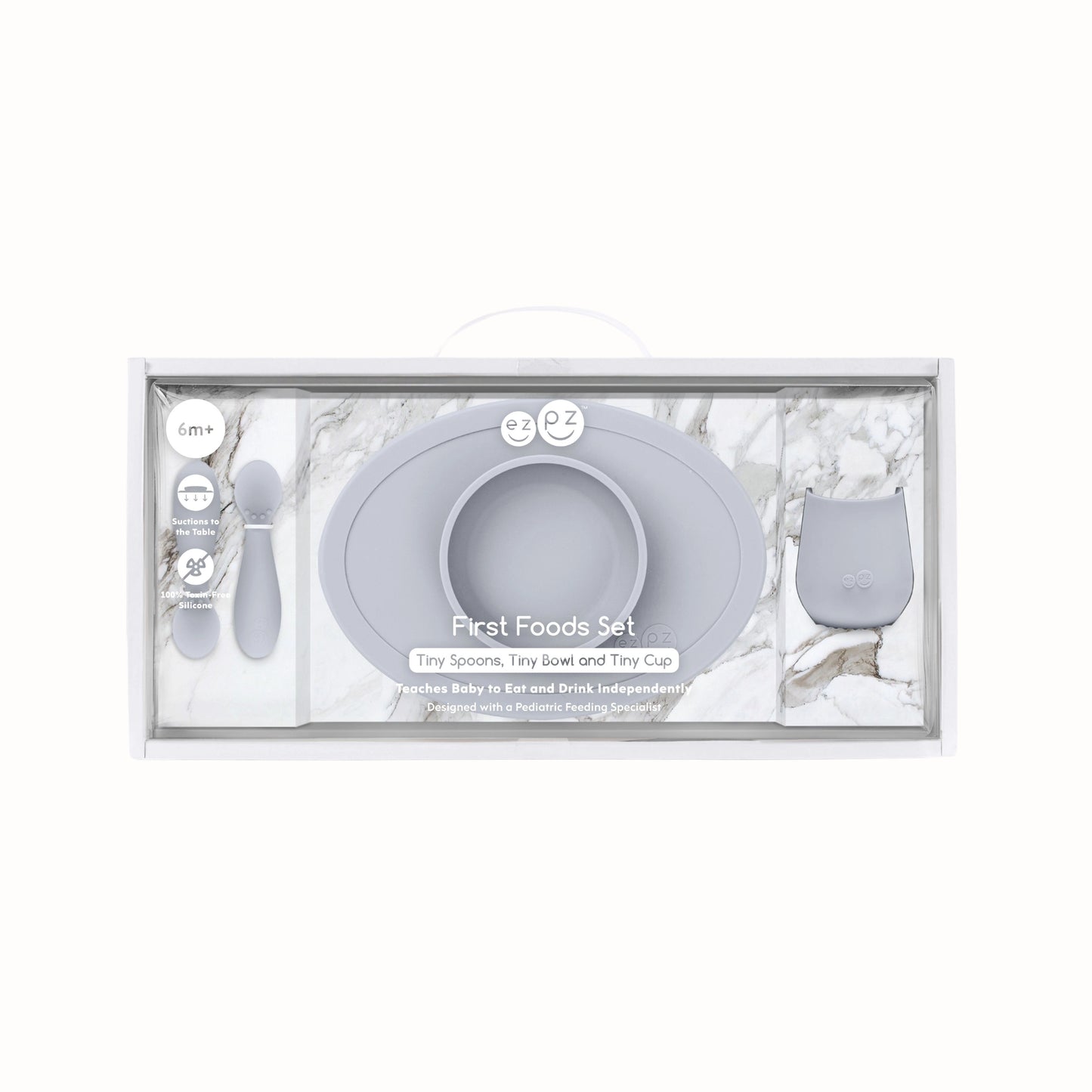 Packaged silicone weaning set with a suction bowl, open cup and baby spoons in a soft pewter grey colour for first foods and self-feeding.
