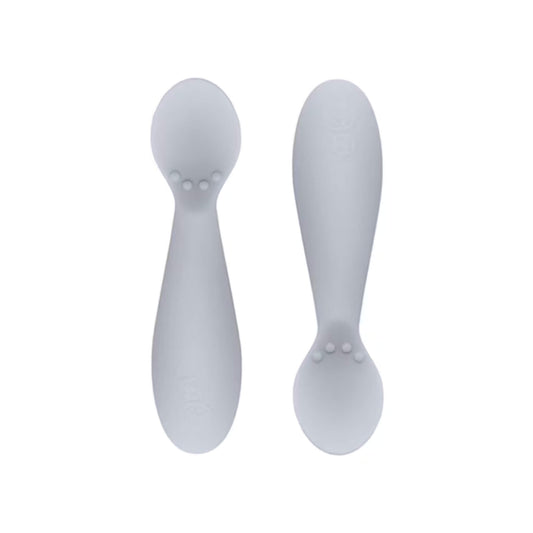 Ezpz Tiny Spoons in blush pink, a pair of silicone infant training spoons with shallow heads and textured bumps near the base.