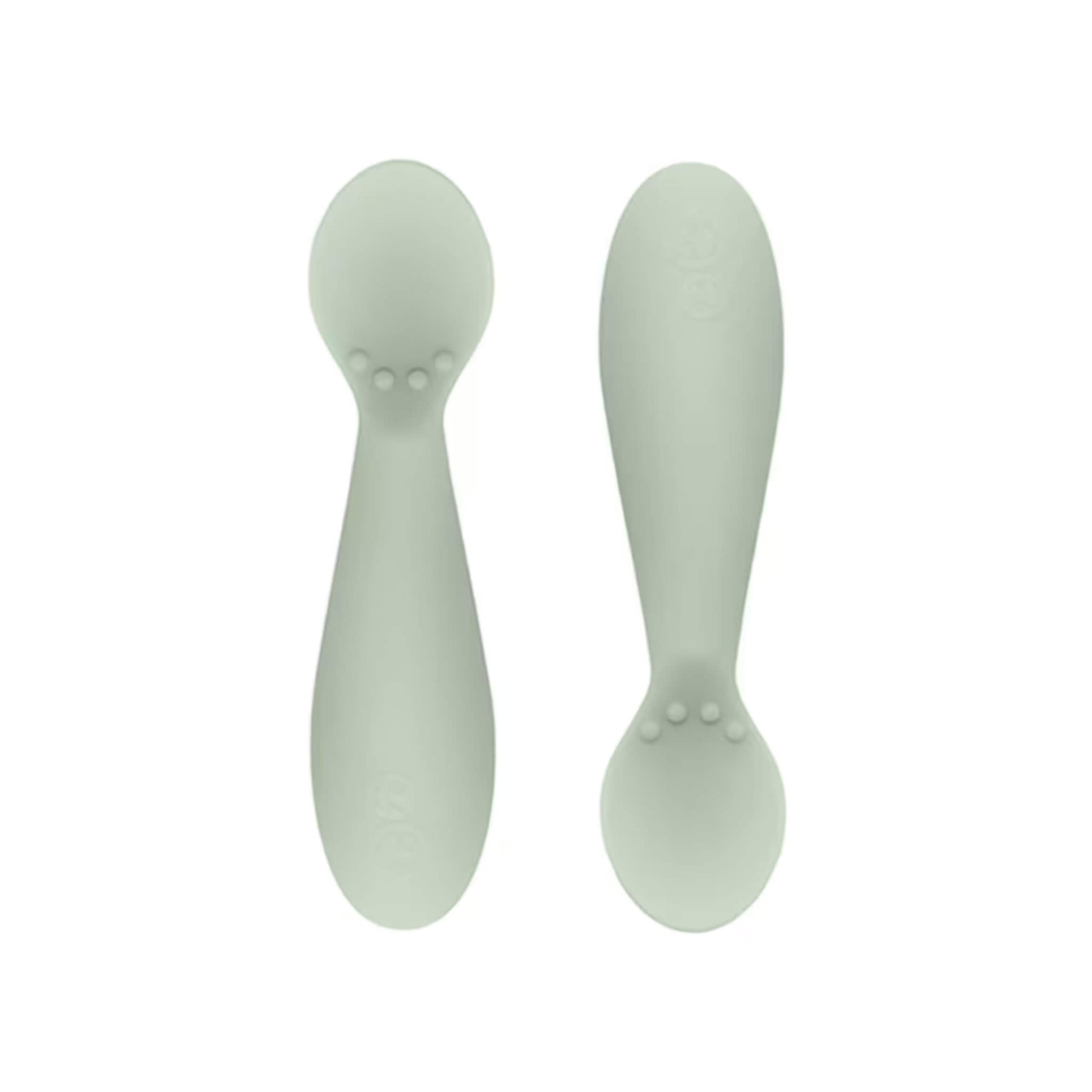 Ezpz Tiny Spoons in sage green, a pair of silicone infant training spoons with shallow heads and textured bumps near the base.