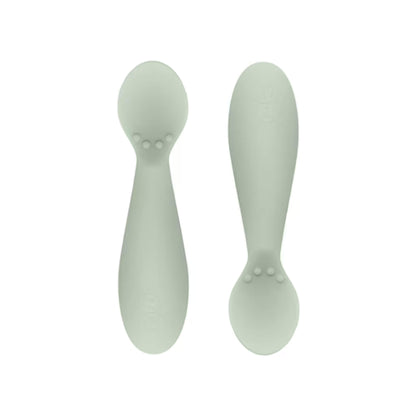 Ezpz Tiny Spoons in sage green, a pair of silicone infant training spoons with shallow heads and textured bumps near the base.