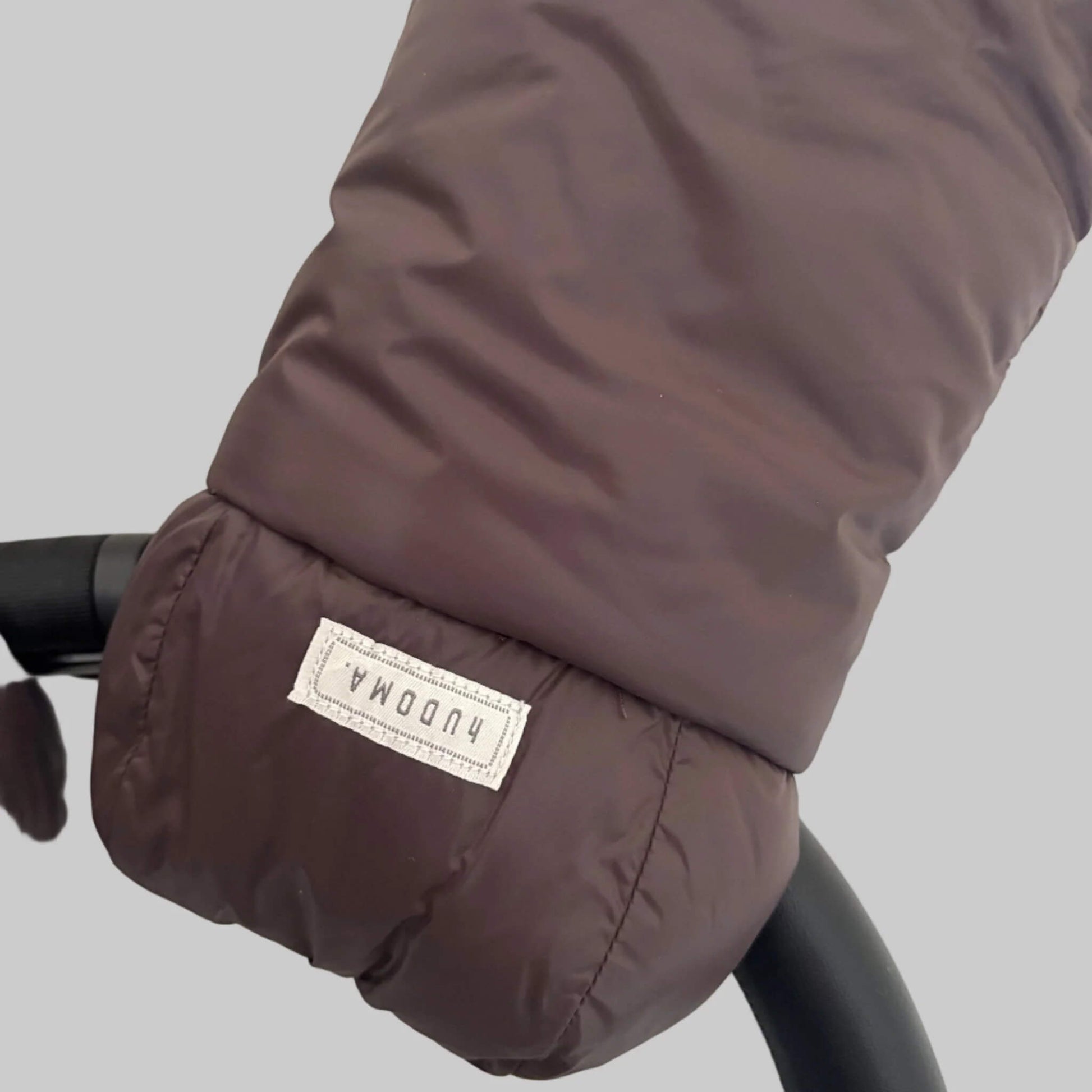 Detailed view of brown pram glove exterior fabric and hUDOMA brand label on the side of the stroller handle.