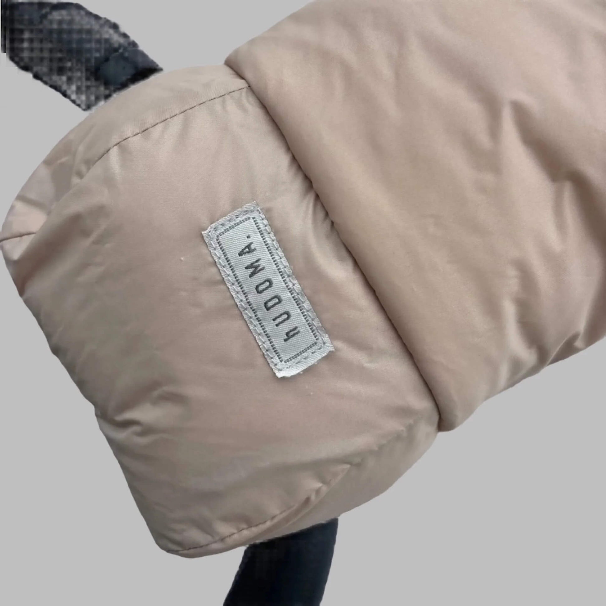 Close-up of beige pram glove exterior with stitched hUDOMA brand label on the side of a stroller handle.