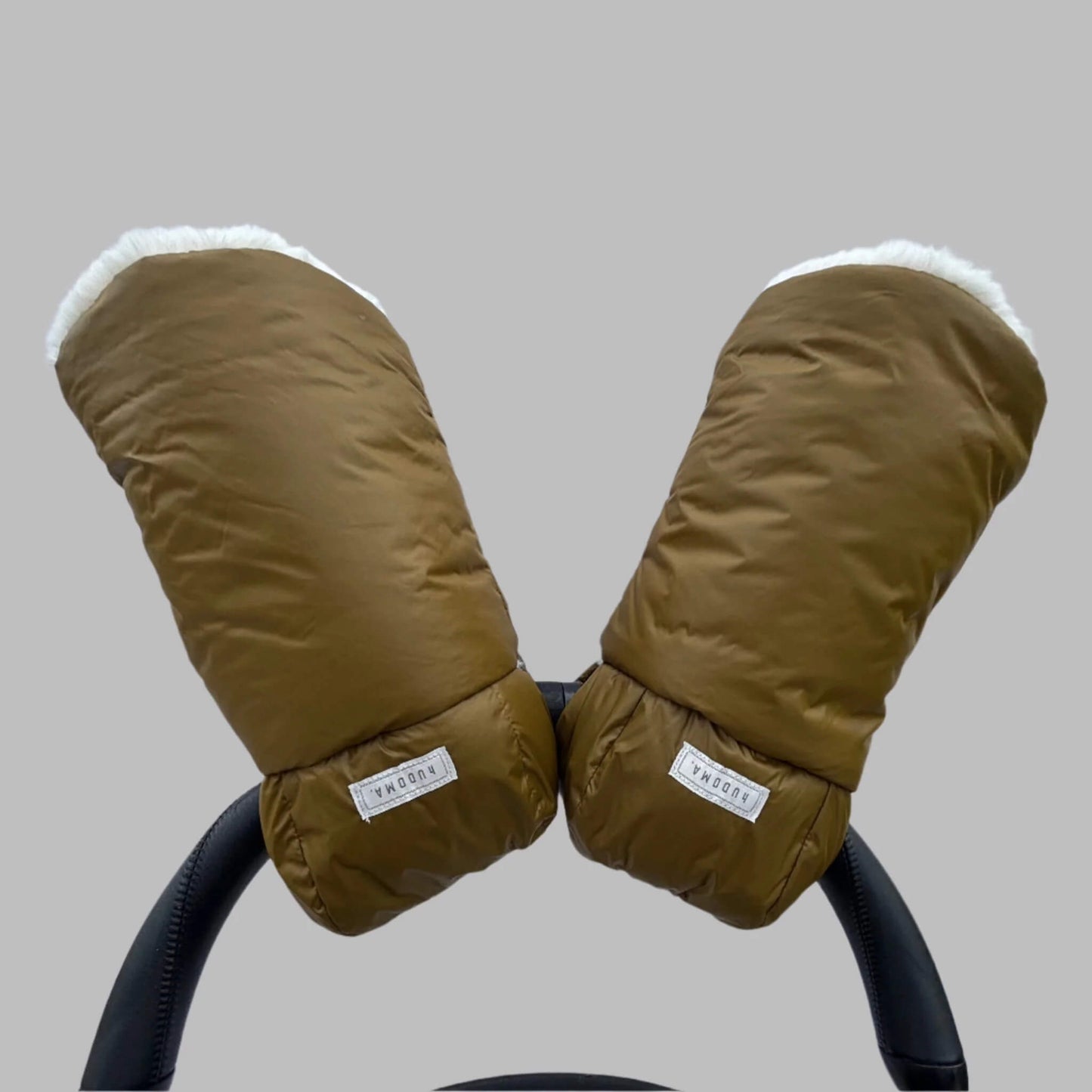 Greenwich Green hUDOMA Pram Gloves attached to a stroller handle, showing both gloves with visible brand labels and soft faux fur lining inside.