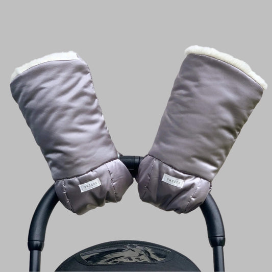 A pair of hUDOMA Pram Gloves in SoHo Silver attached to a black pushchair handle, lined with soft white fleece for comfort and warmth.