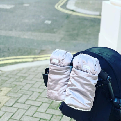 Grey pram gloves fitted to a stroller handle on a city pavement background.