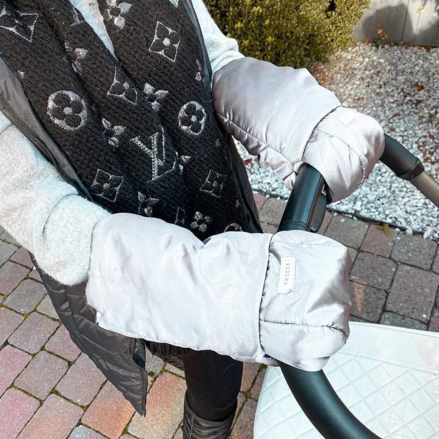 Person wearing silver-grey gloves on a pushchair handle while walking outdoors.