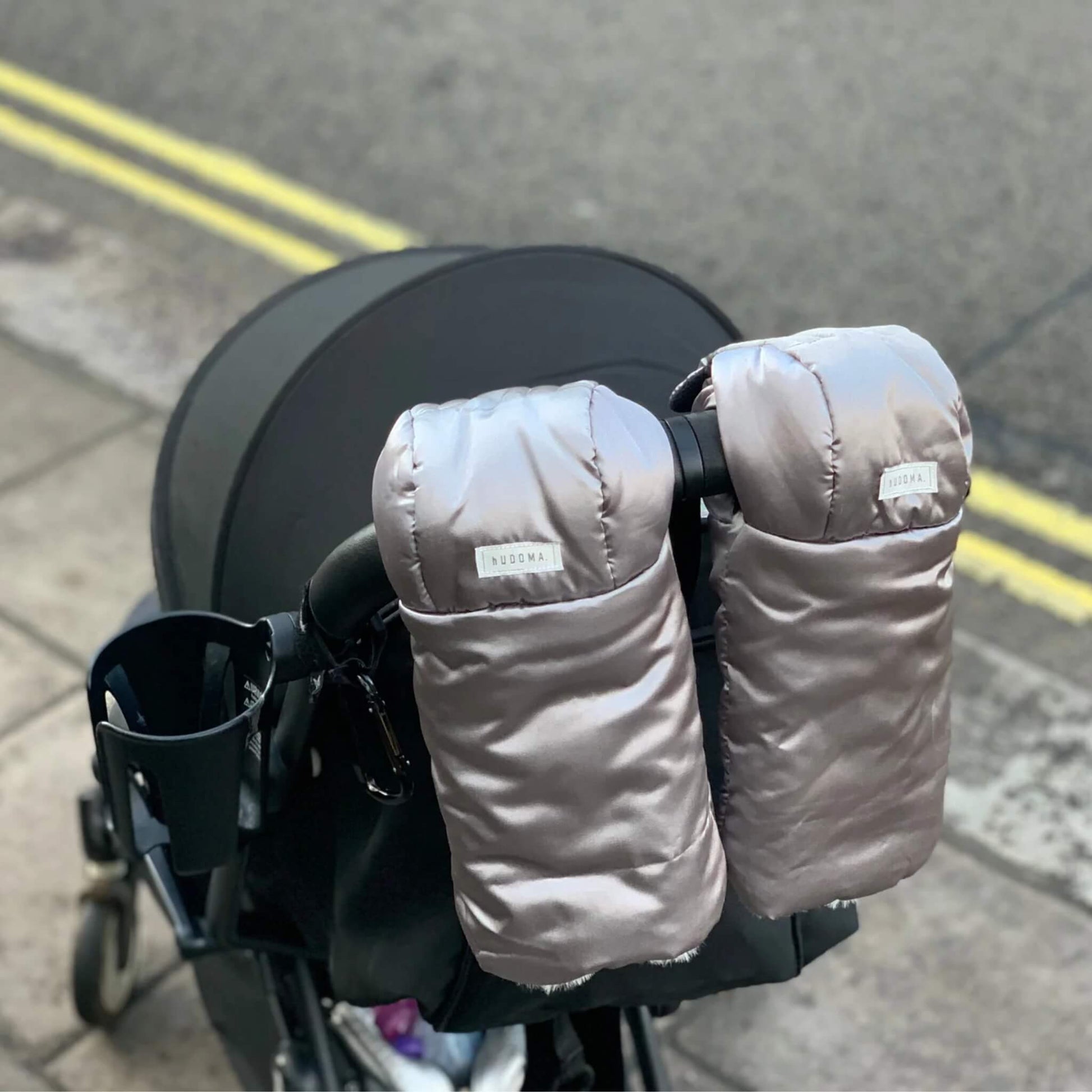 Pram gloves attached to a modern stroller handle on a quiet street.
