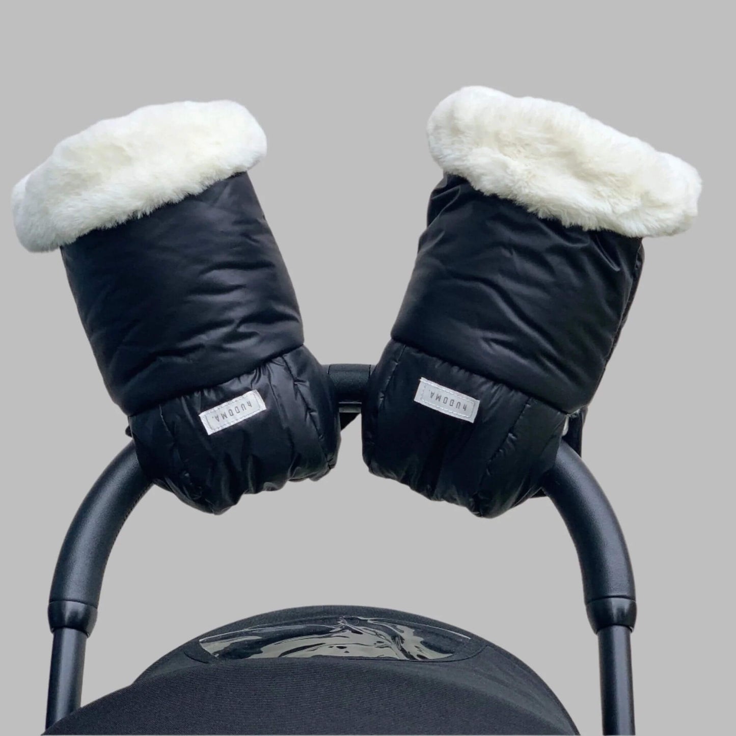 Front-facing view of Pram Gloves securely attached to a stroller handle, showcasing their black exterior and plush white faux fur lining for ultimate warmth and style during winter walks.