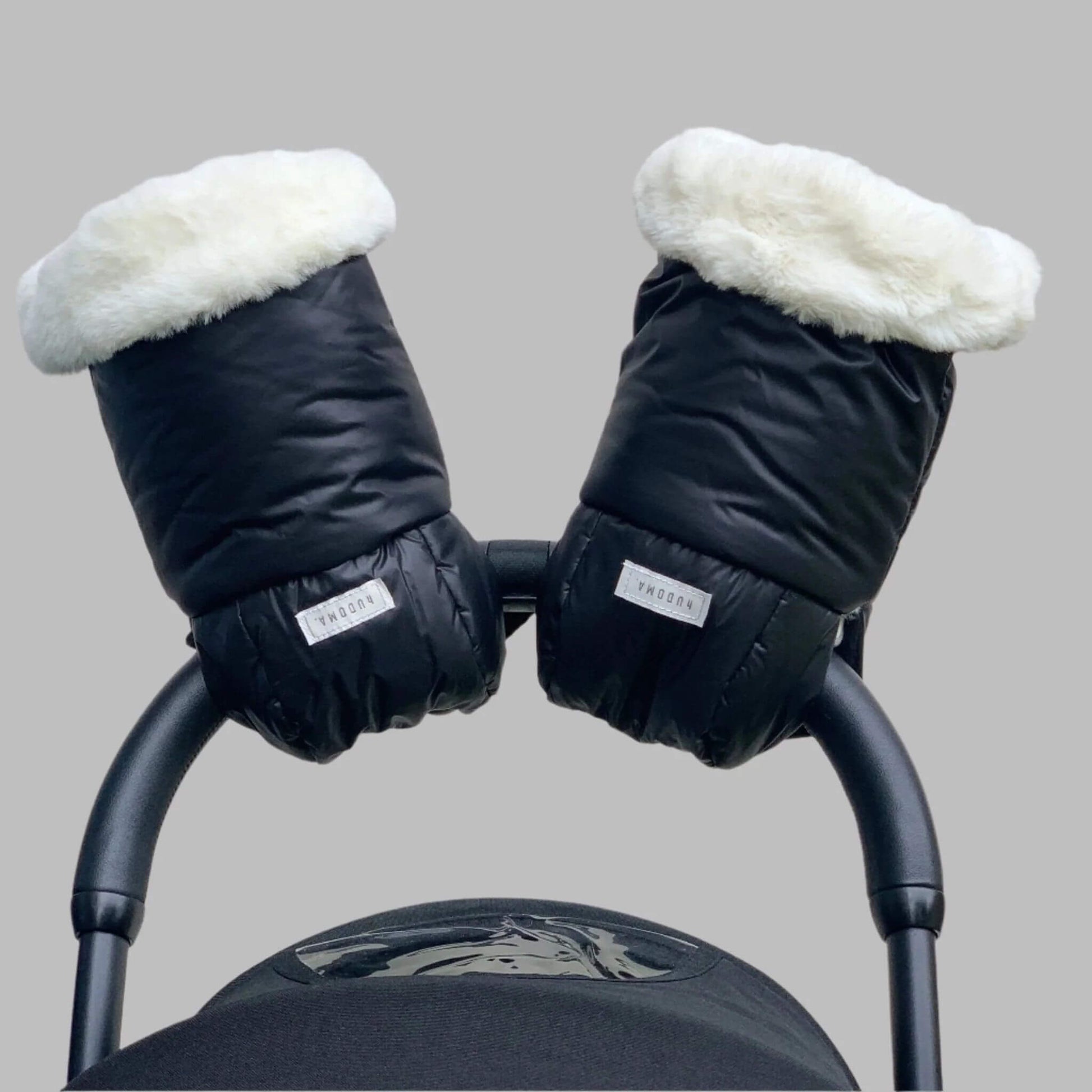 Front-facing view of Pram Gloves securely attached to a stroller handle, showcasing their black exterior and plush white faux fur lining for ultimate warmth and style during winter walks.
