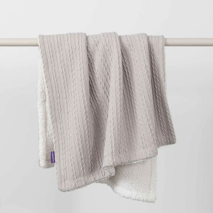Grey cable-knit baby blanket with sherpa fleece reverse, draped over a white rail to show both textures.
