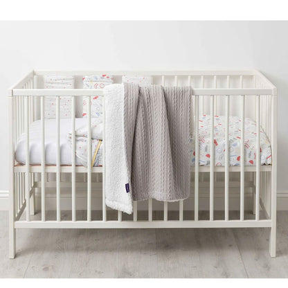 Sherpa-lined baby blanket in grey draped over the side of a white cot, styled with patterned bedding inside.