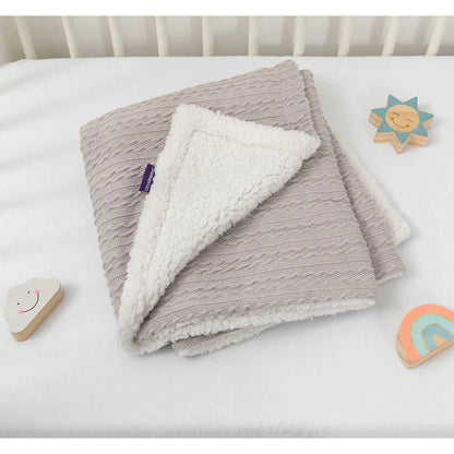 Folded grey sherpa baby blanket resting on a white mattress with wooden toys nearby, showing its soft fleece underside.