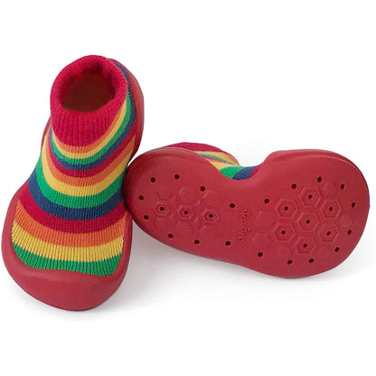 One multi-coloured sock-style baby shoe upright next to a second shoe turned on its side, showing a textured rubber sole with grip pattern.